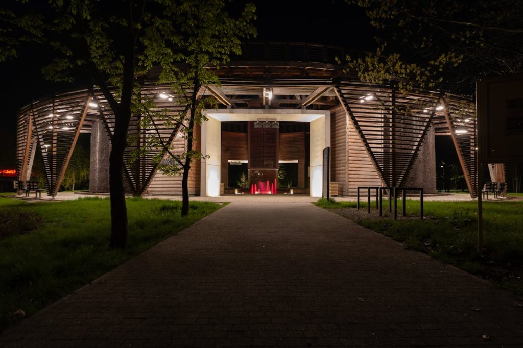 A striking wooden architectural structure illuminated at night in Poland, surrounded by trees.