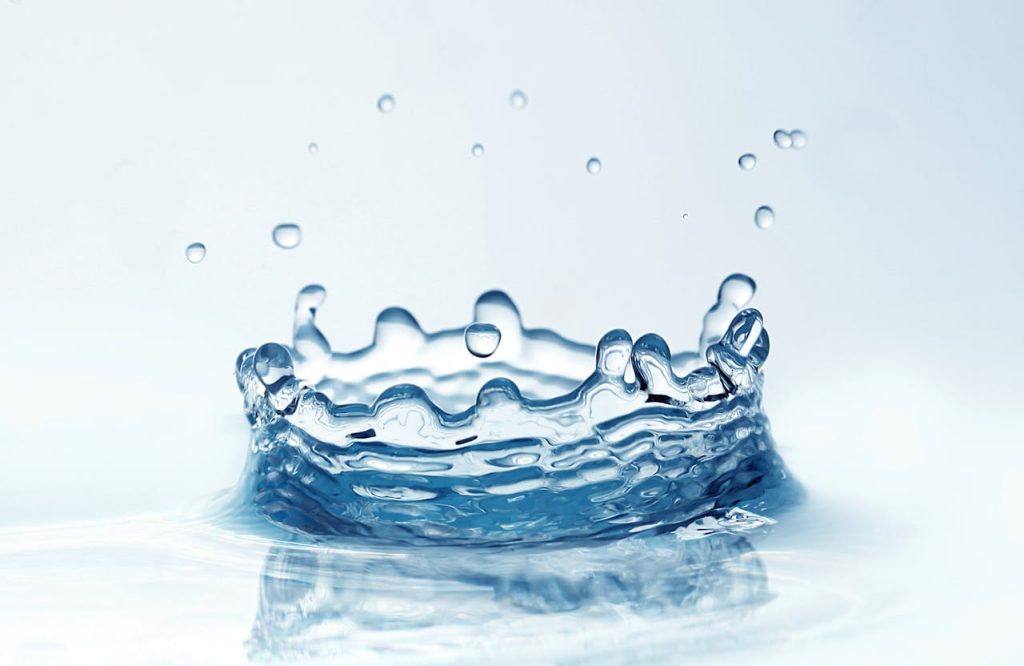 Dynamic close-up of a water droplet splash on a white background, showcasing clarity and motion.